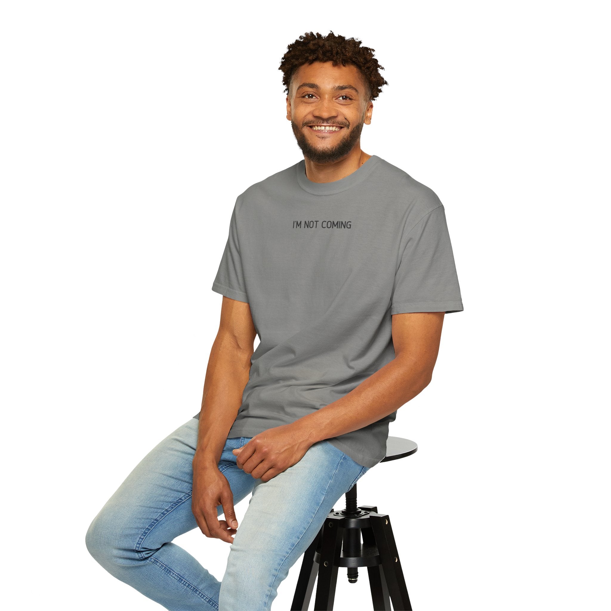 Man sitting on a stool wearing a gray t-shirt with text and light blue jeans.