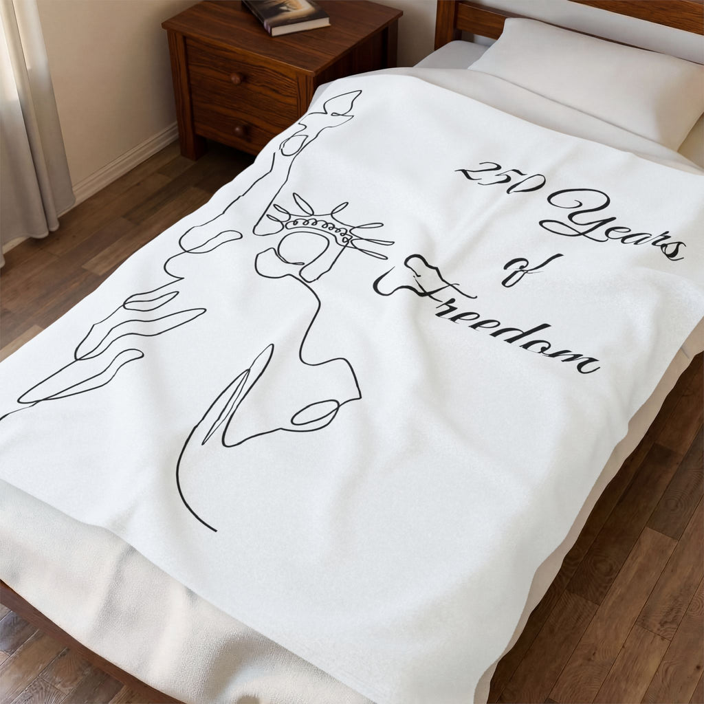 A white fleece blanket with a black continuous line art design of the Statue of Liberty and the text '250 Years of Freedom', shown on a bed in a bedroom setting.