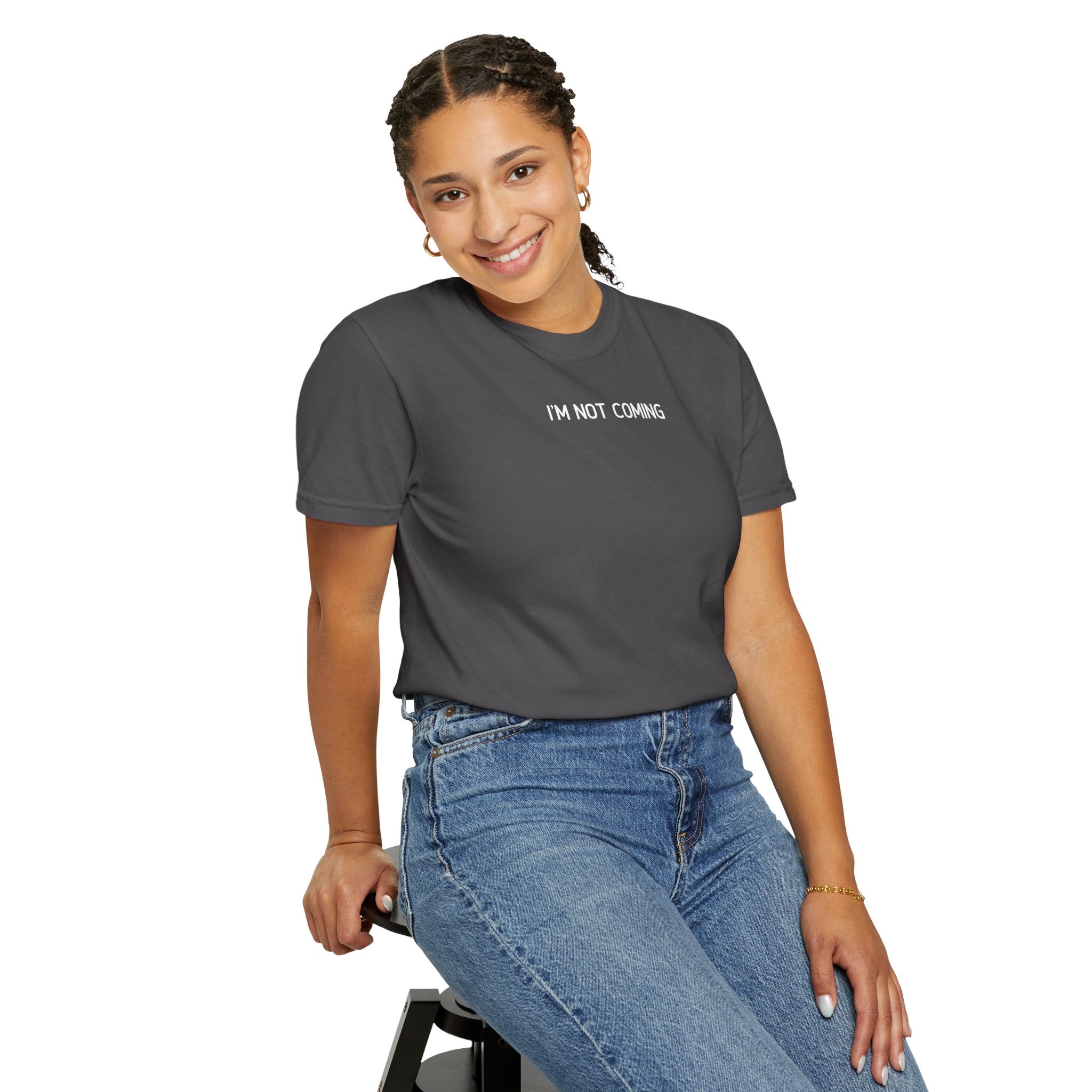 Woman wearing a graphite t-shirt with 'I'M NOT COMING' text and blue jeans, sitting on a stool against a white background.